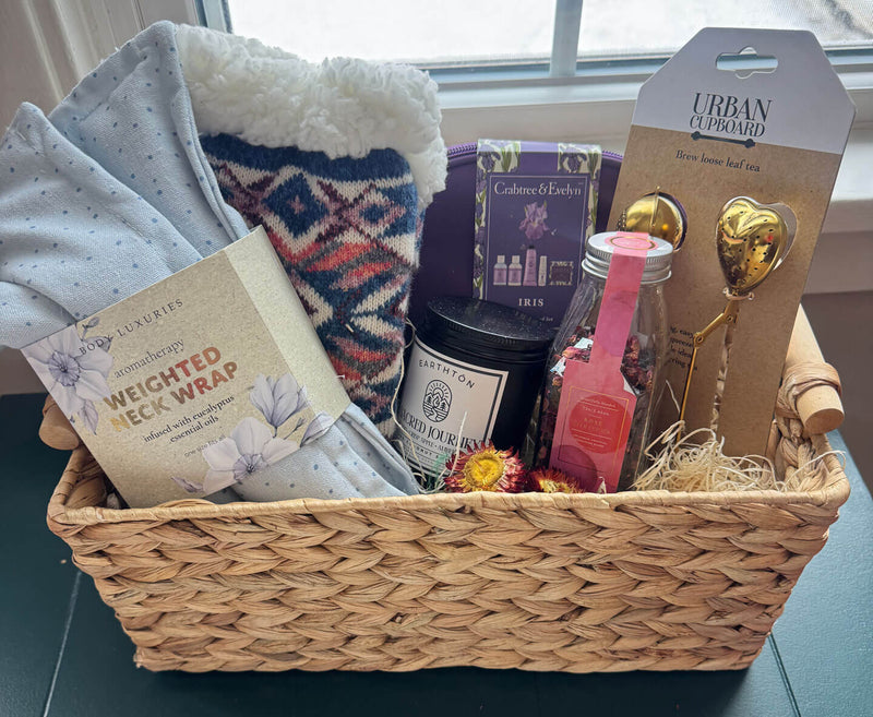 Rooted in Rest Cozy Wellness Gift basket with various items including a weighted neck wrap, candles, and a loose leaf tea strainer.